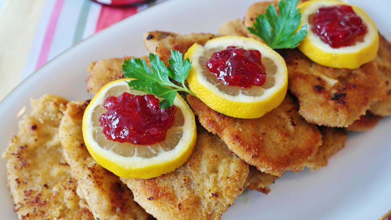 Frittelle di fegato dorate e croccanti appoggiate su carta assorbente bianca, con superficie bruciata color marrone scuro, impilate su un piatto bianco, contorno di limone fresco