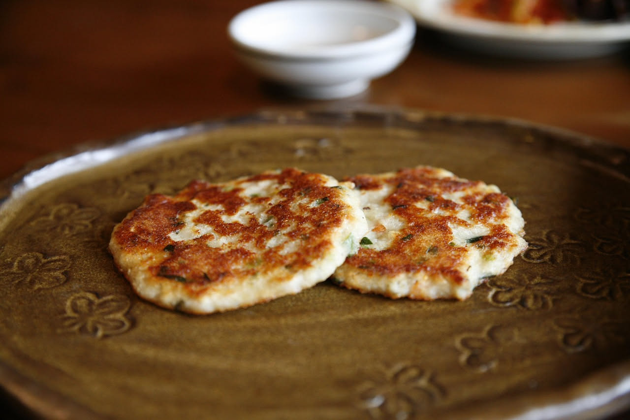 Frittelle di riso salate dorate e croccanti disposte su un piatto bianco, con una superficie irregolare e bollicine visibili, accompagnate da prezzemolo fresco
