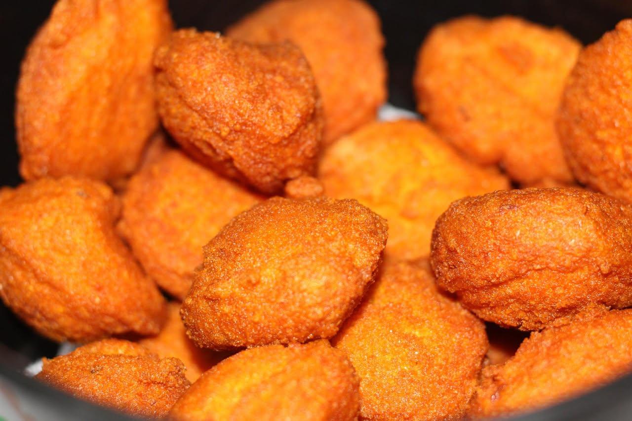 Frittelle di zucca dorate su un piatto bianco, croccanti in superficie, spolverizzate di zucchero e accompagnate da una ciotola di miele liquido