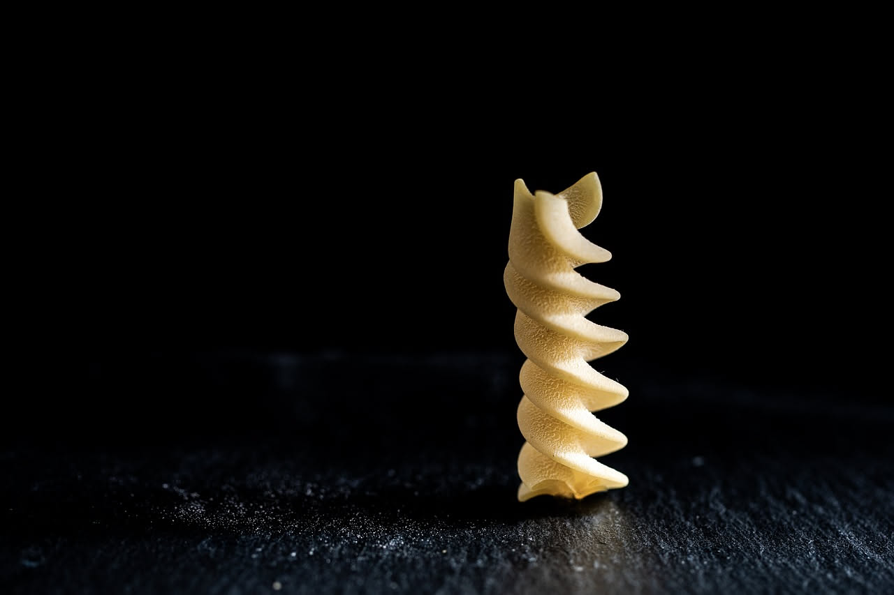 Fusilli al sugo di caccia in piatto bianco, pasta ricoperta di sugo marrone scuro e denso, piccoli pezzi di carne visibile, grana di Parmigiano grattugiata in superficie, fondo del piatto ben pulito