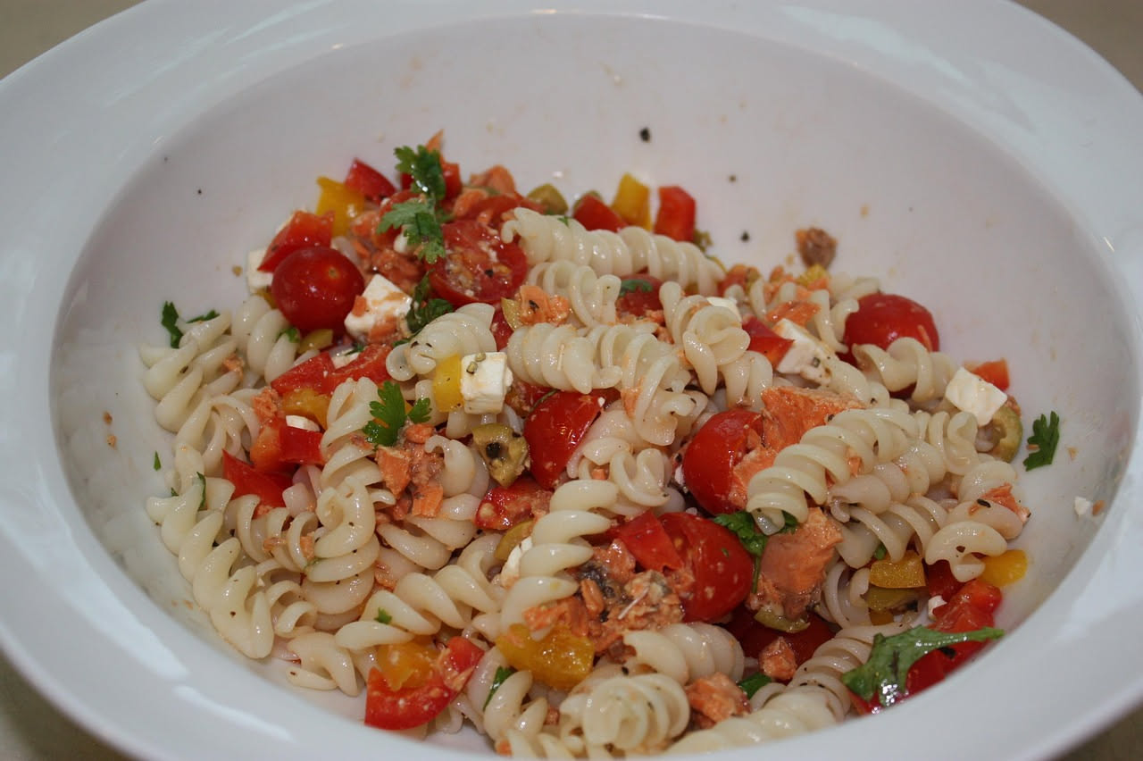 Piatto di fusilli bianchi conditi con sugo rosso di pomodoro e pesce spada in bocconcini, guarnito con basilico fresco verde e un filo di olio d'oliva