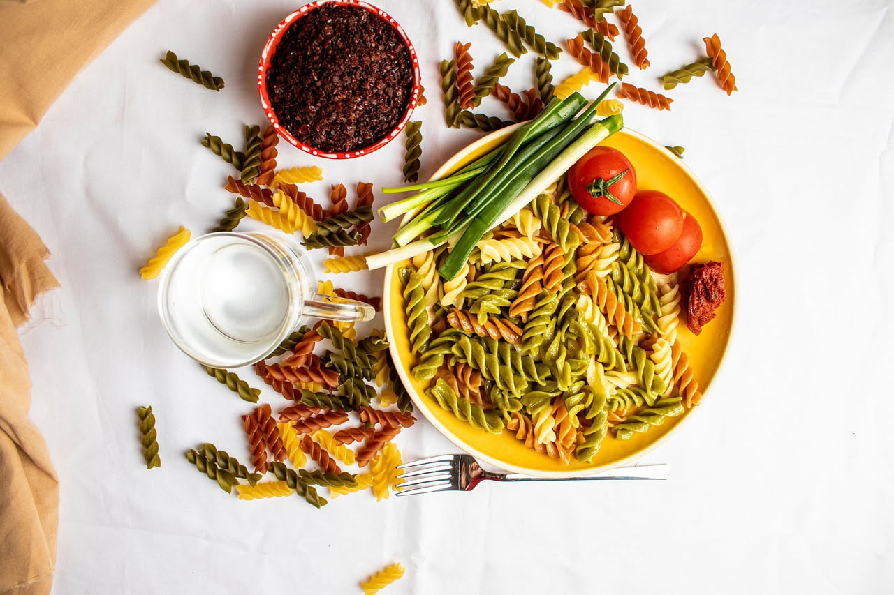 Piatto di fusilli al sugo di pomodoro rosso vivo, conditi con olio extravergine lucido, foglia di basilico fresco verde scuro, parmigiano grattugiato bianco in rilievo sulla superficie, serviti in pia