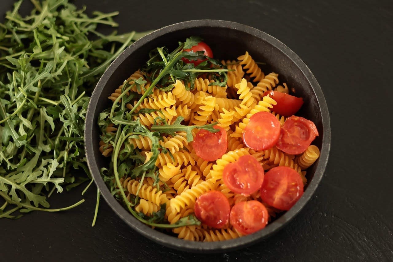 Piatto fondo di fusilli gialli raccolti con melanzane scure, pezzi di carne ragù, pomodori rossi, grana grattugiato bianco e basilico verde fresco in cima