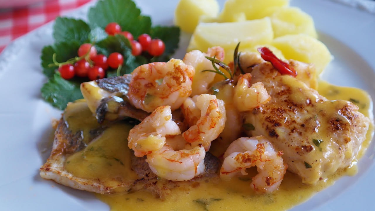 Gamberetti rosati saltati in padella con fettine di limone giallo, prezzemolo fresco tritato e gocce di olio d'oliva, serviti su un piatto bianco