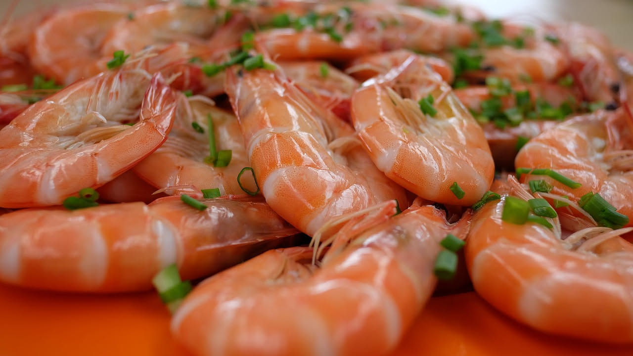 Gamberoni rosa e bianchi cotti al forno su piatto bianco, con spicchi di limone, prezzemolo fresco e gocce d'olio d'oliva