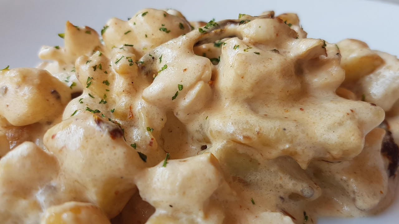 Piatto di ceramica bianca con gnocchi ricoperti di ragù rosso, melanzane scure, formaggio grattugiato bianco e basilico verde, fotografato dall'alto con forchetta di acciaio inox