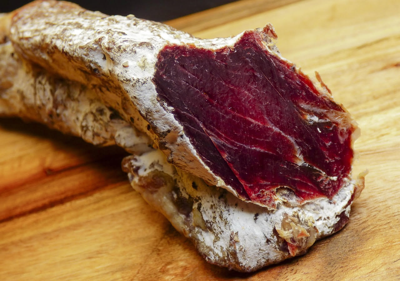 Fette di guancia salata maremma tagliate finemente, di colore rosso scuro con parti bianche di grasso, disposte su un tagliere di legno con un coltello affiancato