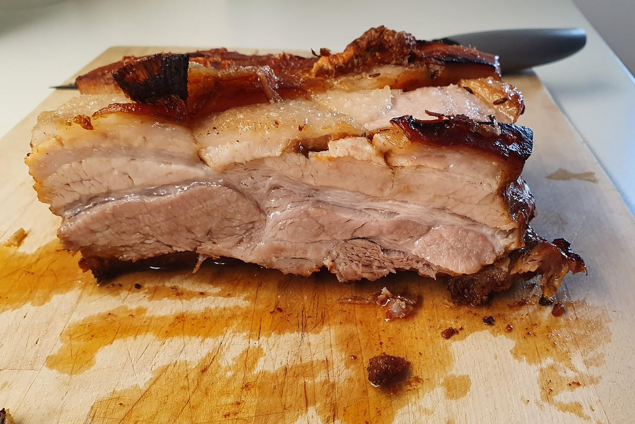 Guanciale arrostito in forno su una teglia, con la crosta dorata e lucida, contornato da erbe aromatiche fresche e aglio