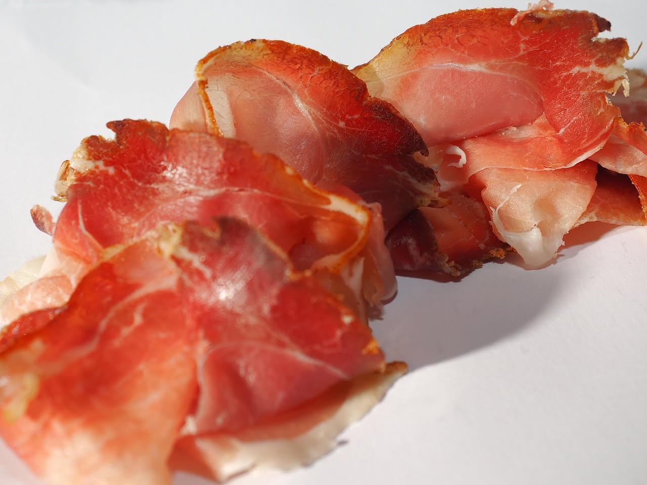 Fette sottili di guanciale crudo affettato disposte a ventaglio su un piatto bianco, con colore rosa perlato e grasso marmorizzato, accanto a pane tostato e un bicchiere di vino rosso