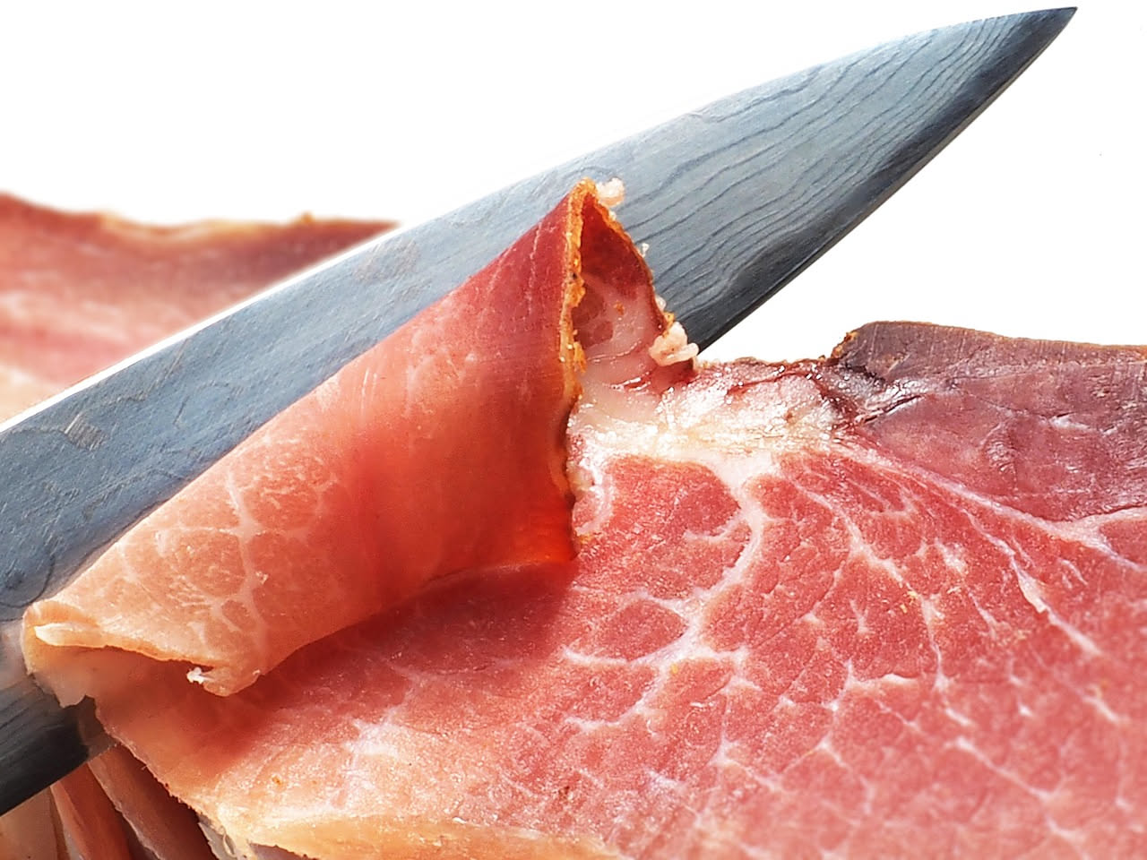 Guanciale dell'Emilia affettato su un tagliere di legno, con fette rosa e bianche, accanto a due chicchi di pepe nero e una foglia di rosmarino fresco