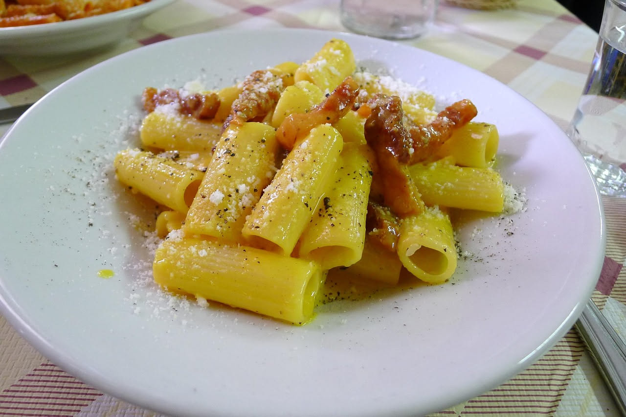 Fette sottili di guanciale marchigiano rosa pallido con striature di grasso, disposte a ventaglio su un piatto bianco, con accanto pane tostato e un bicchiere di vino rosso