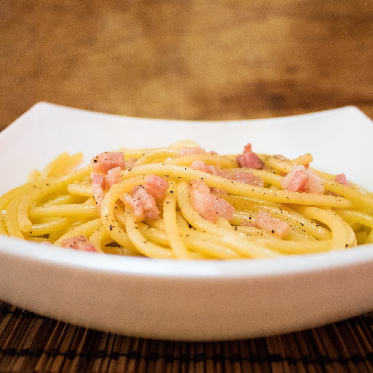 Fette di guanciale stagionato di colore rosato con striature bianche di grasso, disposte su un tagliere di legno con pepe nero macinato