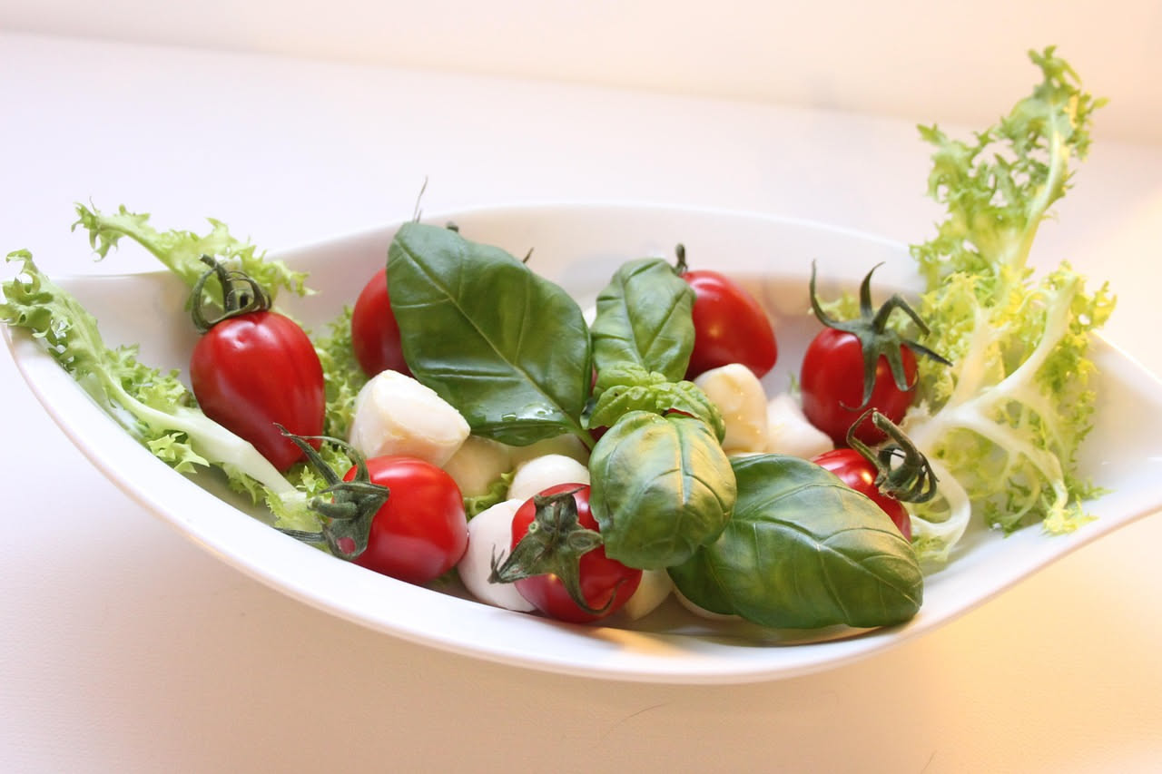 Insalata di pasta fredda con penne, pomodori rossi, cetrioli verdi, mozzarella bianca a cubetti, prezzemolo fresco e olio d'oliva in una ciotola trasparente, servita su un piatto bianco con bordo azzu