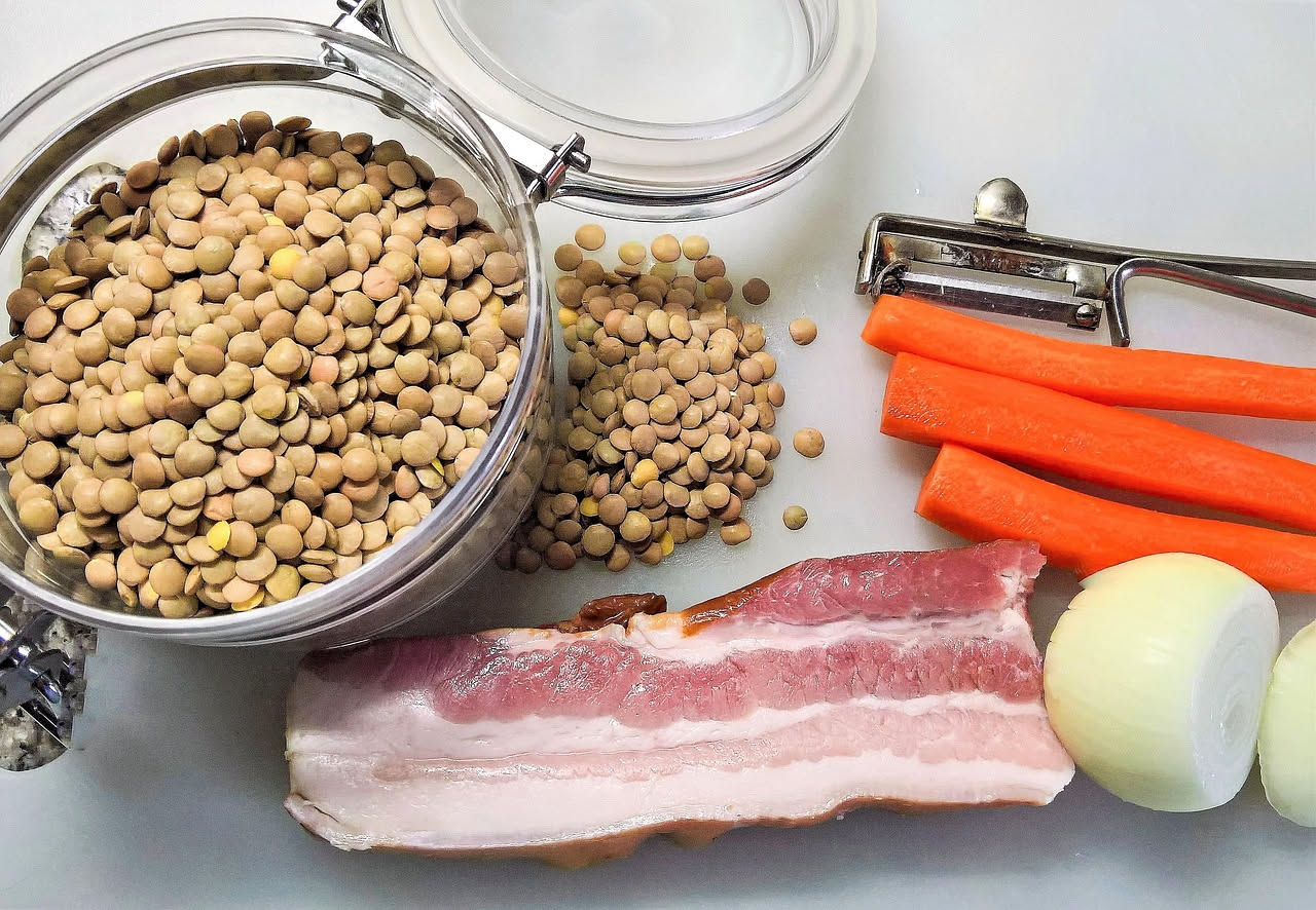 Piatto di lagane con lenticchie: strisce di pasta gialla ondulate ricoperte di lenticchie rosse e gialle in un sugo di cipolla e pomodoro, condite con olio extravergine, su piatto bianco di ceramica