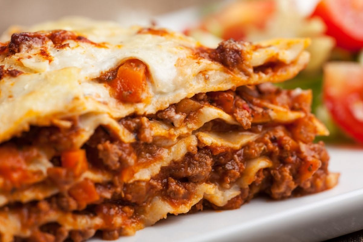 Lasagne alla Siciliana tagliate nel piatto, strati visibili di pasta gialla, ragù rosso scuro, melanzane color melanzana scuro, formaggio dorato in superficie, guarnite con basilico fresco