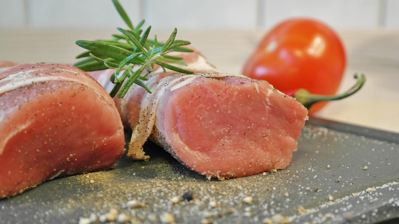 Lonza di maiale affettata su un piatto bianco con contorno di verdure radicate caramellate e pan di spezie, superficie lucida e colore marrone dorato