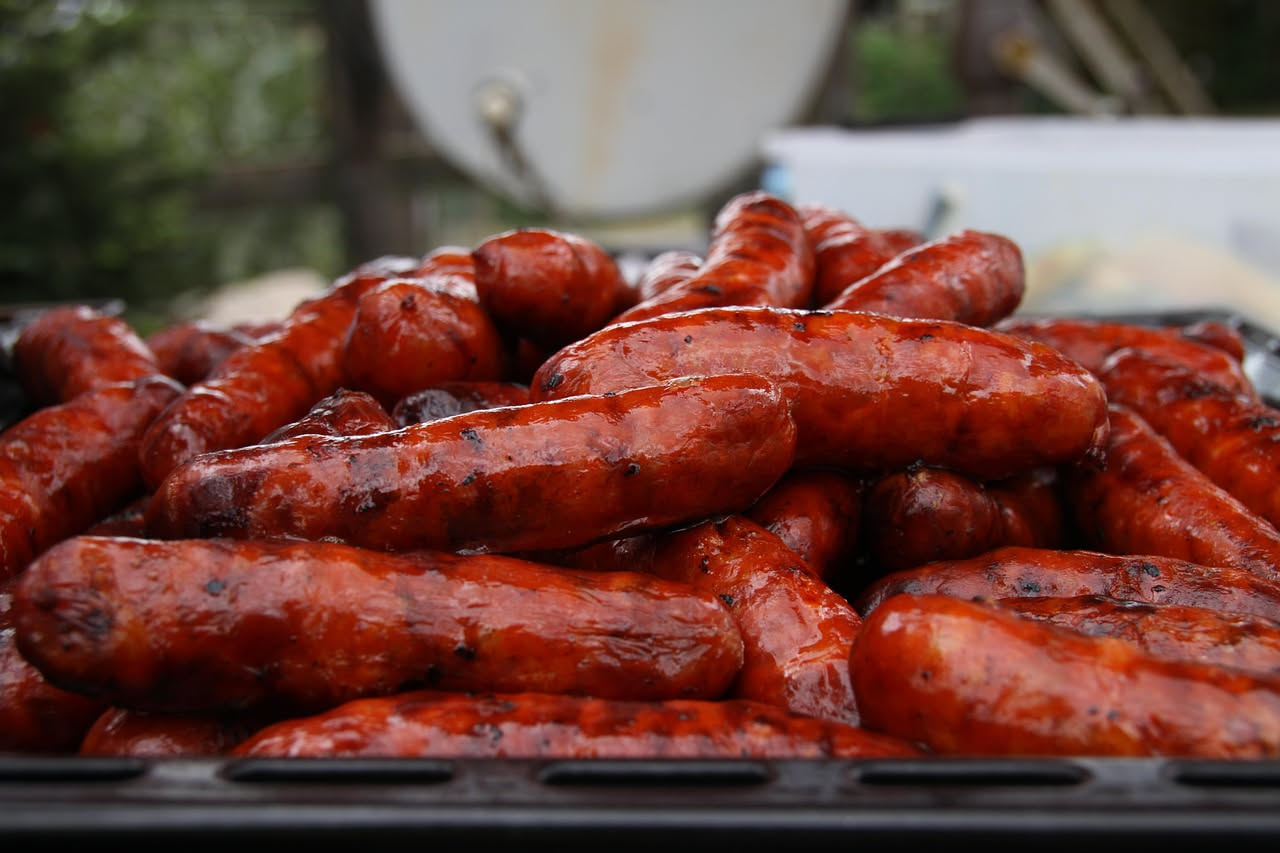 Luganega affumicata dorata e croccante in padella di ferro, con sfumature marroni e buccia leggermente abbrustolita, contorno di cipolla rosso pallido e rosmarino fresco