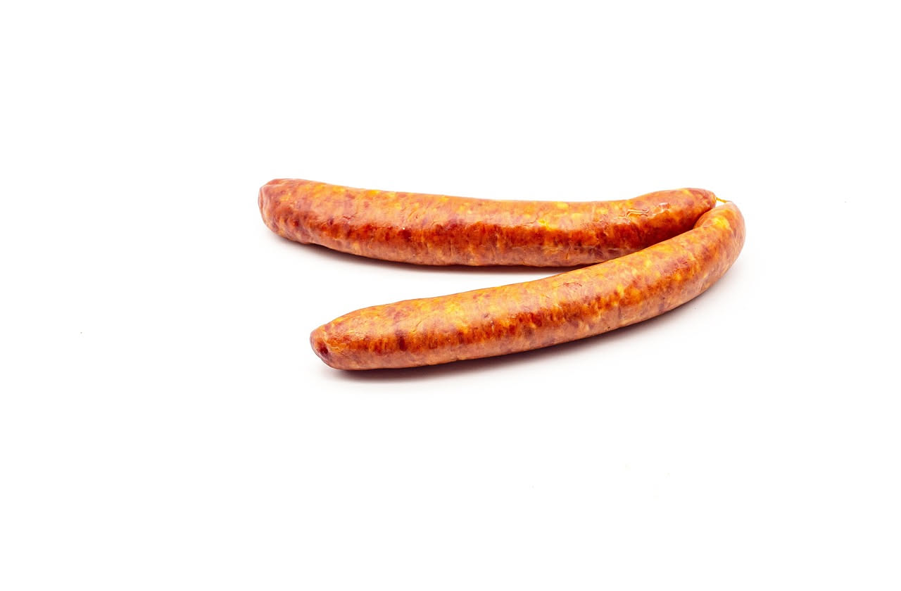 Luganega vicentina cotta in un piatto bianco, salsiccia a spirale stretta color marrone dorato con piccole gocce trasparenti di grasso, affiancata da un lime tagliato a spicchi e due rametti di salvia