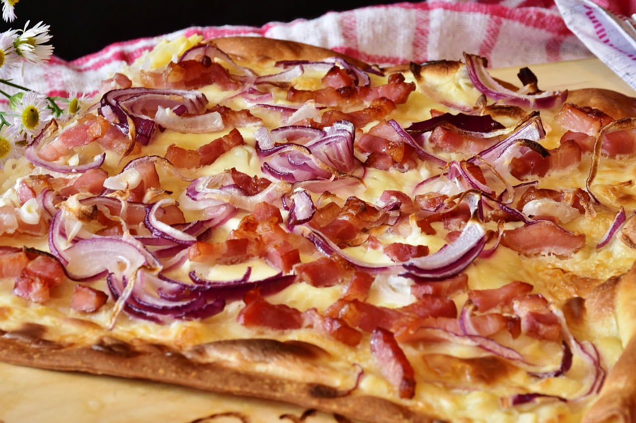 Piatto bianco con luganica dorata e cipolla caramellata, guarnito con prezzemolo fresco, accanto a fette di pane tostato
