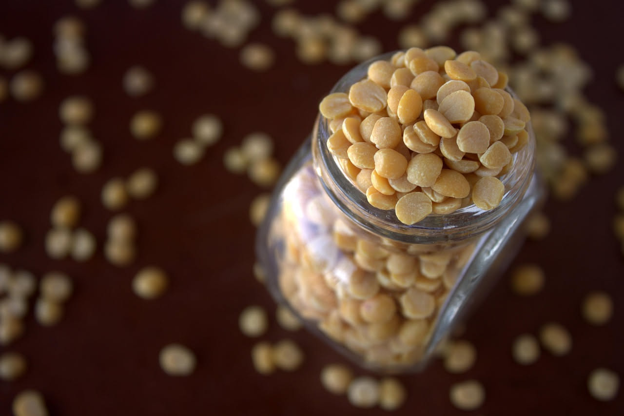 Lupini bianchi e gialli bolliti in una ciotola bianca con acqua salata, alcuni sgusciati e altri ancora con il baccello, su un tavolo di legno