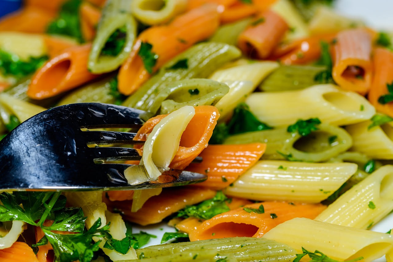 Maccarruni ca' pummaruòla nel piatto: pasta ricurva color giallo-ambra coperta di sugo rosso brillante, guarniti con pochi fili di basilico fresco verde, poggiati su un piatto bianco con orlo sottile