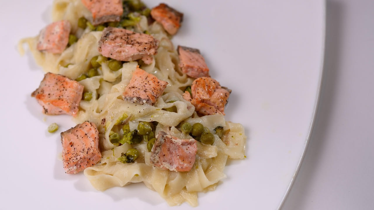 Piatto di maltagliati con zucchine verdi, melanzane viola, pomodori rossi e basilico fresco, servito in una ciotola bianca con un filo di olio d'oliva.