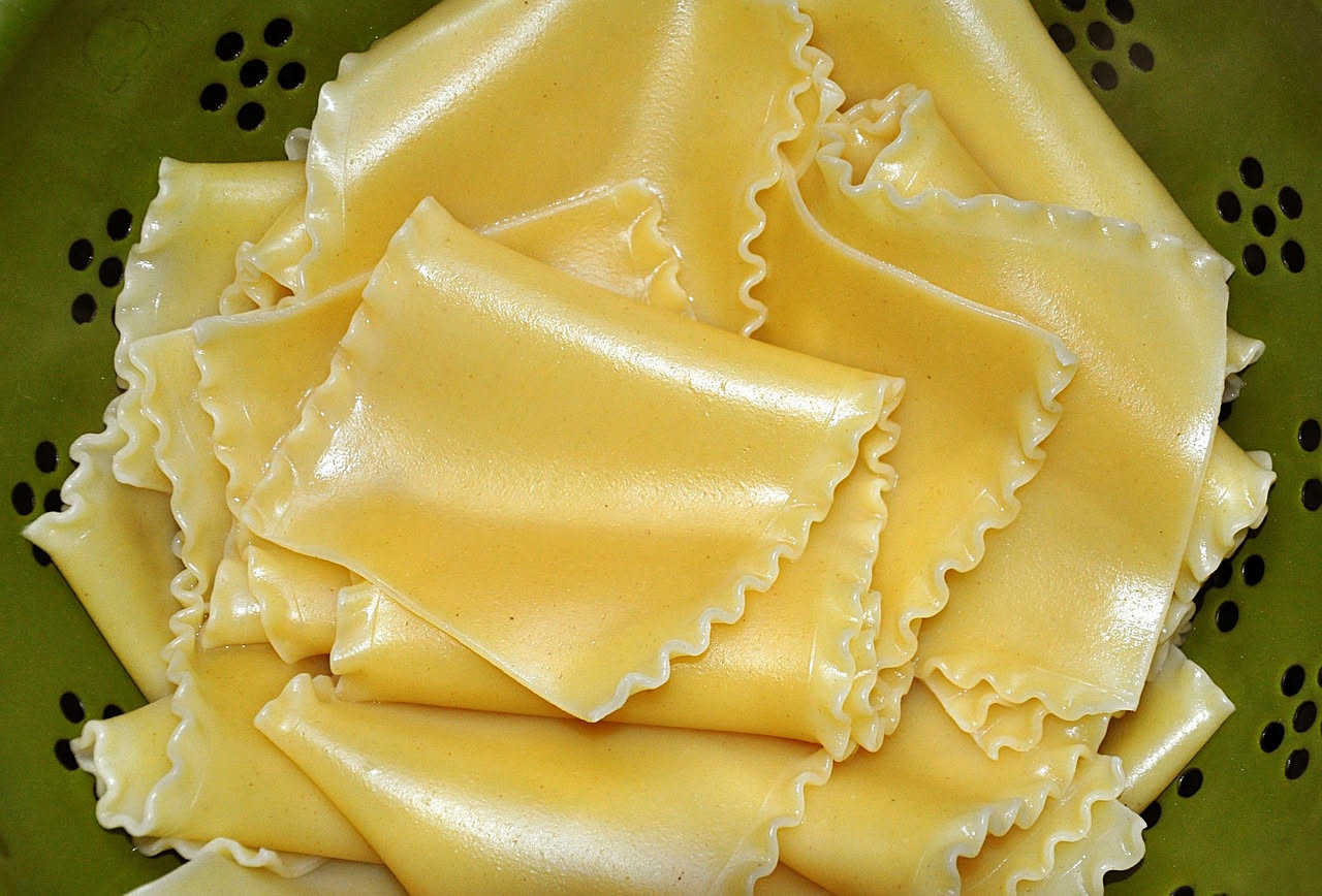 Sei manicotti ripieni di ricotta allineati in pirofila di ceramica bianca, ricoperti di salsa di pomodoro rosso e formaggio gratinato leggermente dorato, con foglie di basilico verde fresco tra i tubi
