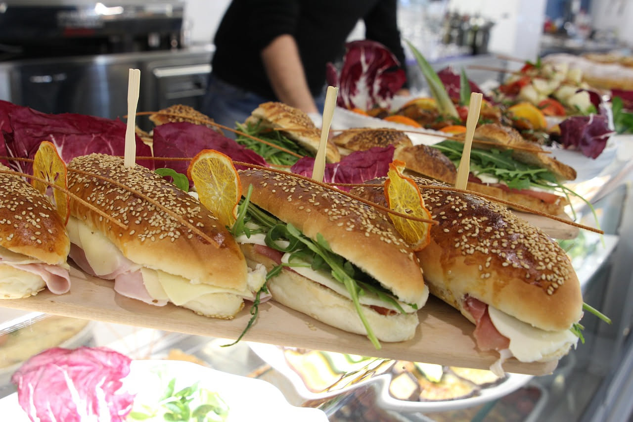 Maritozzo salato aperto mostra interno con mozzarella, prosciutto crudo, rucola e pomodoro su sfondo bianco