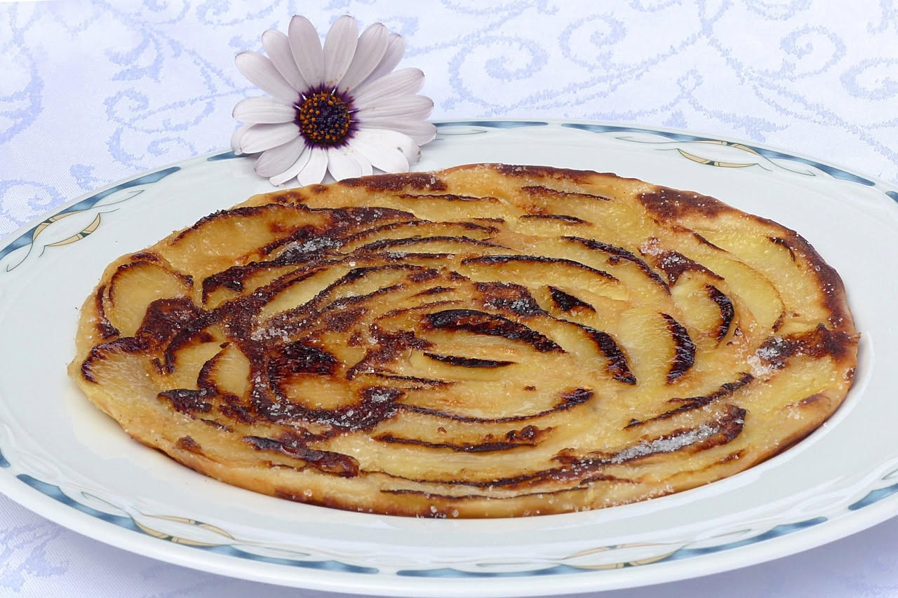 Piatto bianco con fette di formaggio erborinato e composta di mela cotogna dal colore rosso scuro, guarnito con noci tostate e foglie di salvia fresca