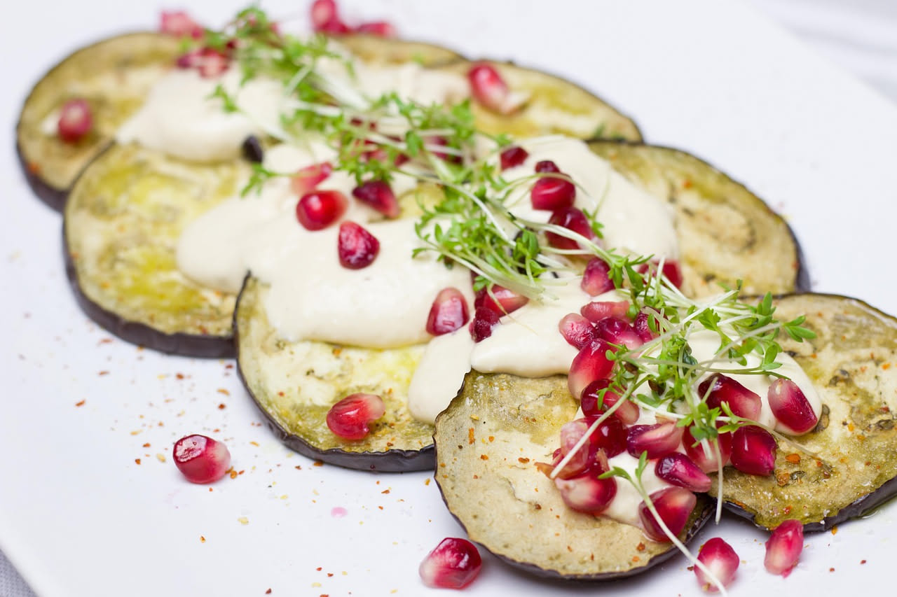 Melanzane fritte disposte in piatto bianco con aceto e menta fresca, colore viola scuro e interno dorato, condimento brillante visibile