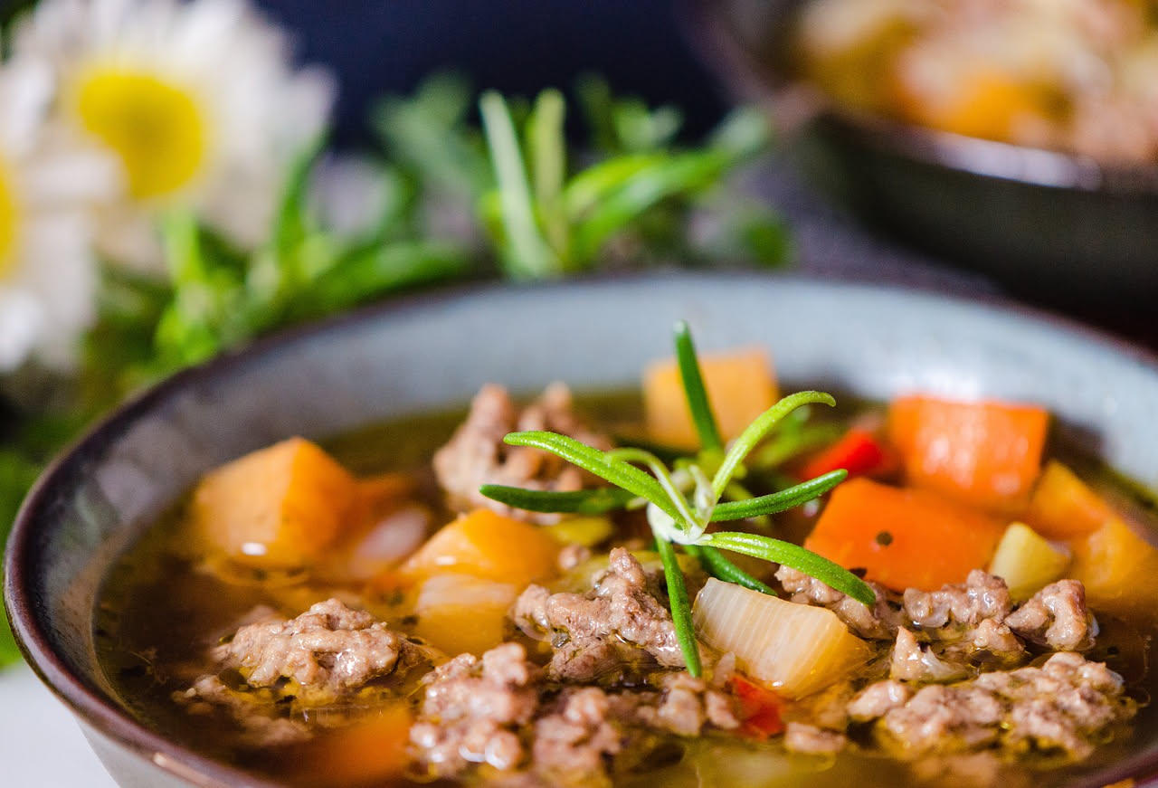 Zuppa mesciua in una ciotola bianca, cremosa e densa, con fagioli, ceci e chicchi di farro visibili, cosparsa di prezzemolo fresco verde, servita con pane tostato a lato