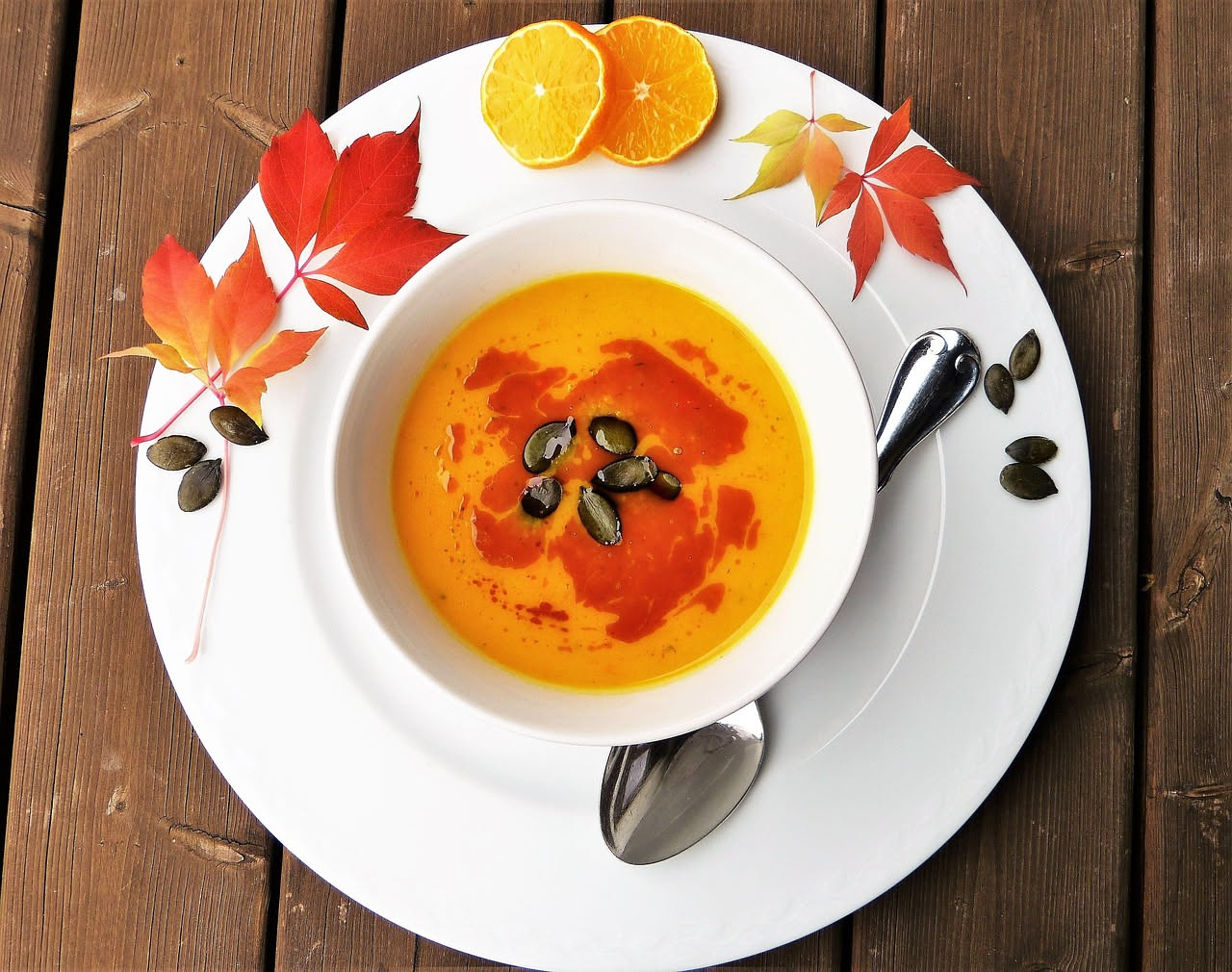 Minestra d'autunno in ciotola bianca, cremosa con pezzetti di zucca arancione, cavolo verde, fagioli bianchi visibili, con cucchiaio in acciaio e pane tostato accanto