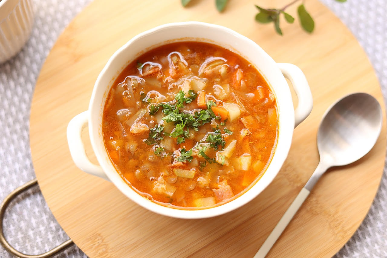 Ciotola di minestra d'orzo fumante con orzo perlato visibile, brodo chiaro color ambra, cubetti di verdure morbide e filo d'olio crudo in superficie, servita in piatto fondo bianco