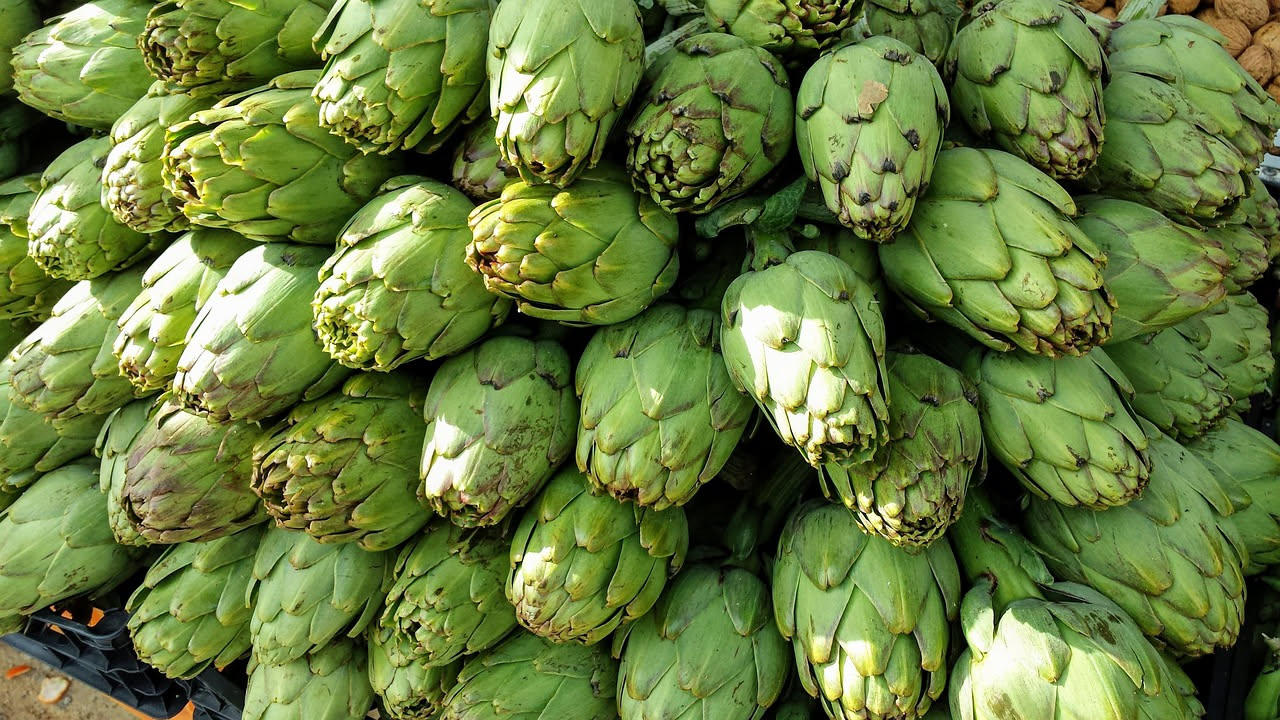 Minestra di carciofini servita in scodella bianca, con carciofini verdi pallido interi, pezzetti di patata dorati, fili di cipolla, olio verde in superficie, su tovaglia bianca di lino
