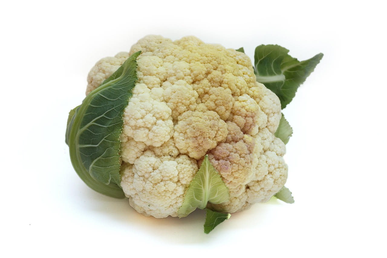 Ciotola di minestra di cavolfiore con pezzi di cavolfiore color crema, patate gialle, brodo trasparente, guarnita con prezzemolo fresco, servita in stoviglie bianche su un tavolo di legno naturale