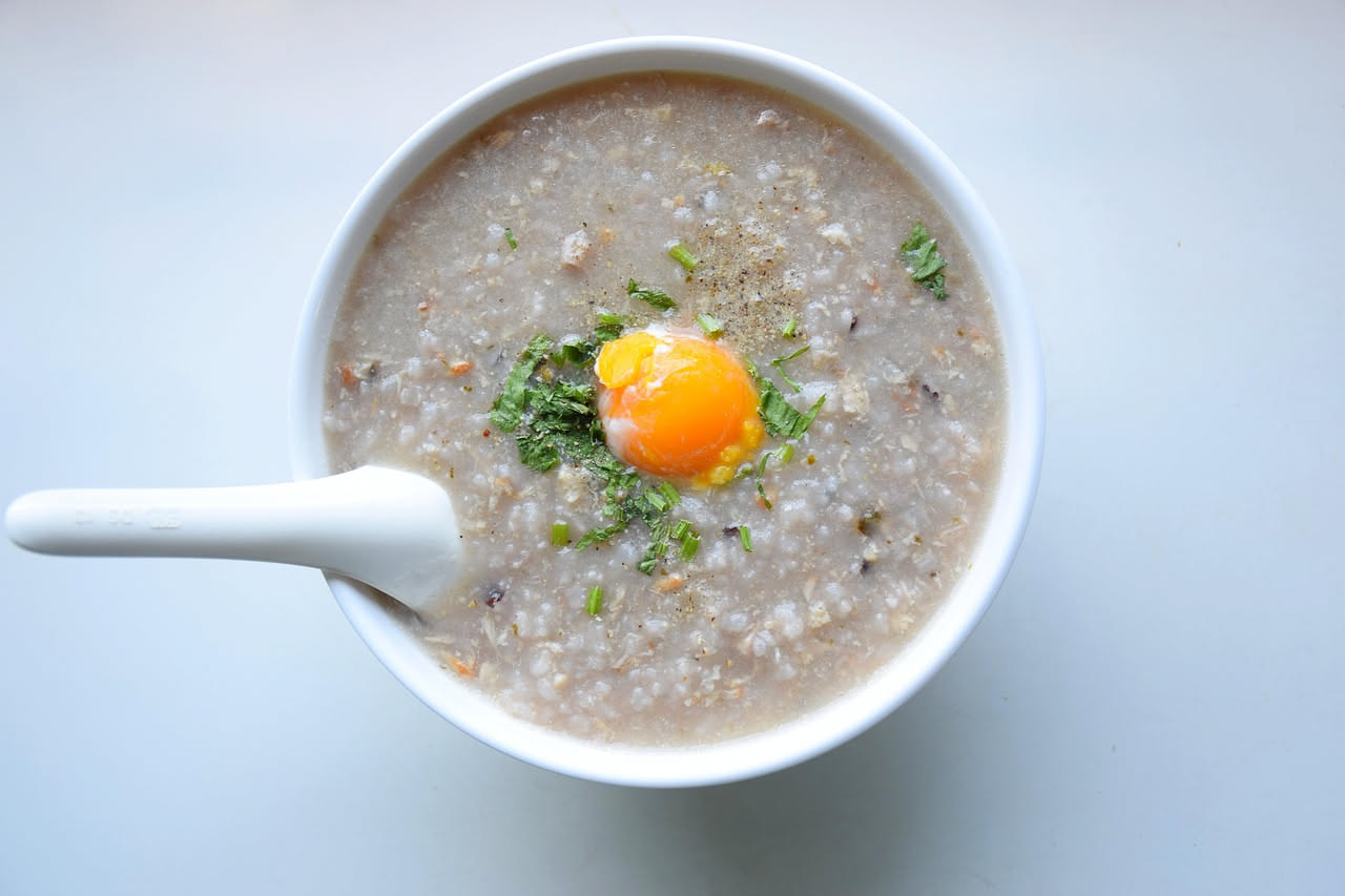 Piatto di minestra di farina e brodo color crema in ciotola bianca, con una cucchiaiata sollevata che mostra la consistenza vellutata, brodo limpido e fumante, servito su tavolo di legno
