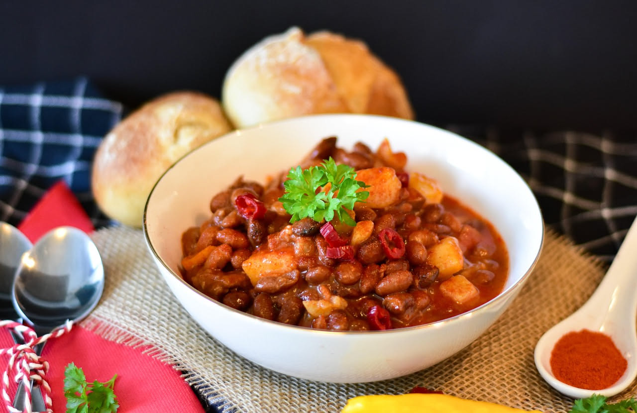 Minestra di farro e fagioli in ciotola di ceramica bianca, brodo trasparente color nocciola con chicchi di farro gonfi, fagioli interi color marrone, carota e sedano affettati, prezzemolo fresco verde