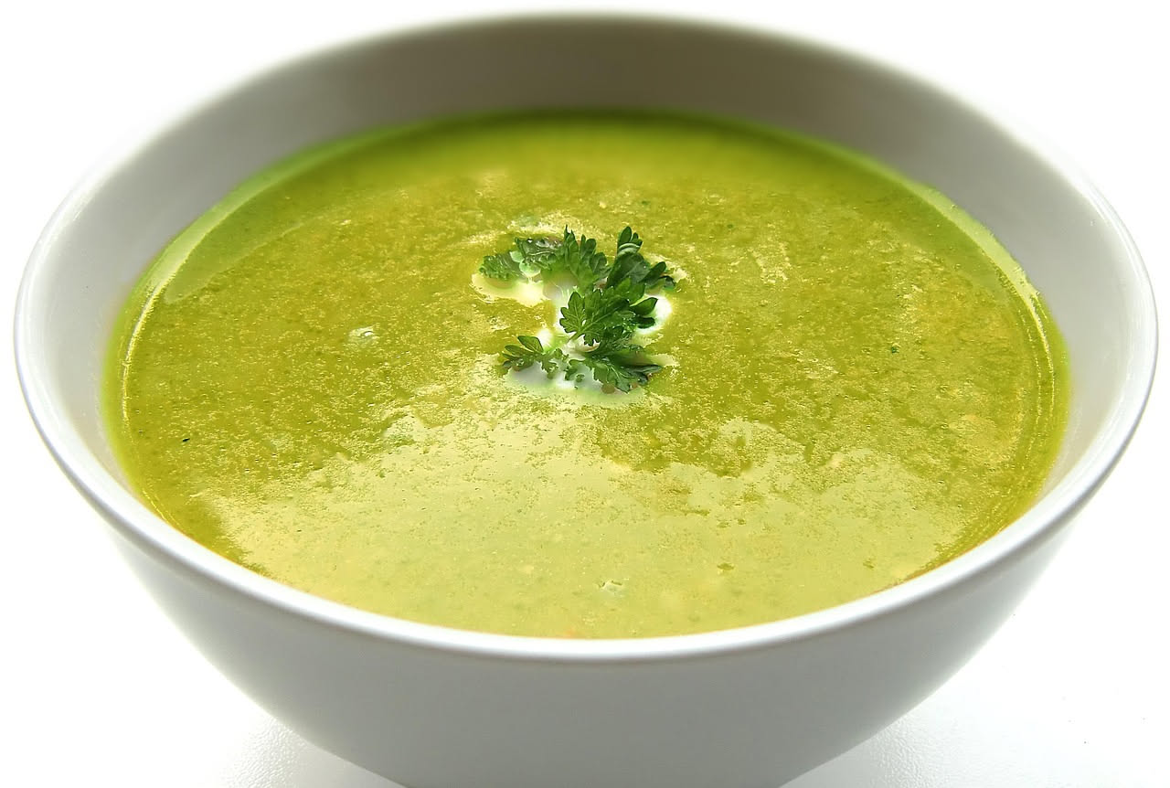 Minestra di fave in ciotola di ceramica bianca, colore verde pallido uniforme, fave integre e sfaldabili visibili in superficie, filo di olio extravergine, pane tostato sul bordo del piatto
