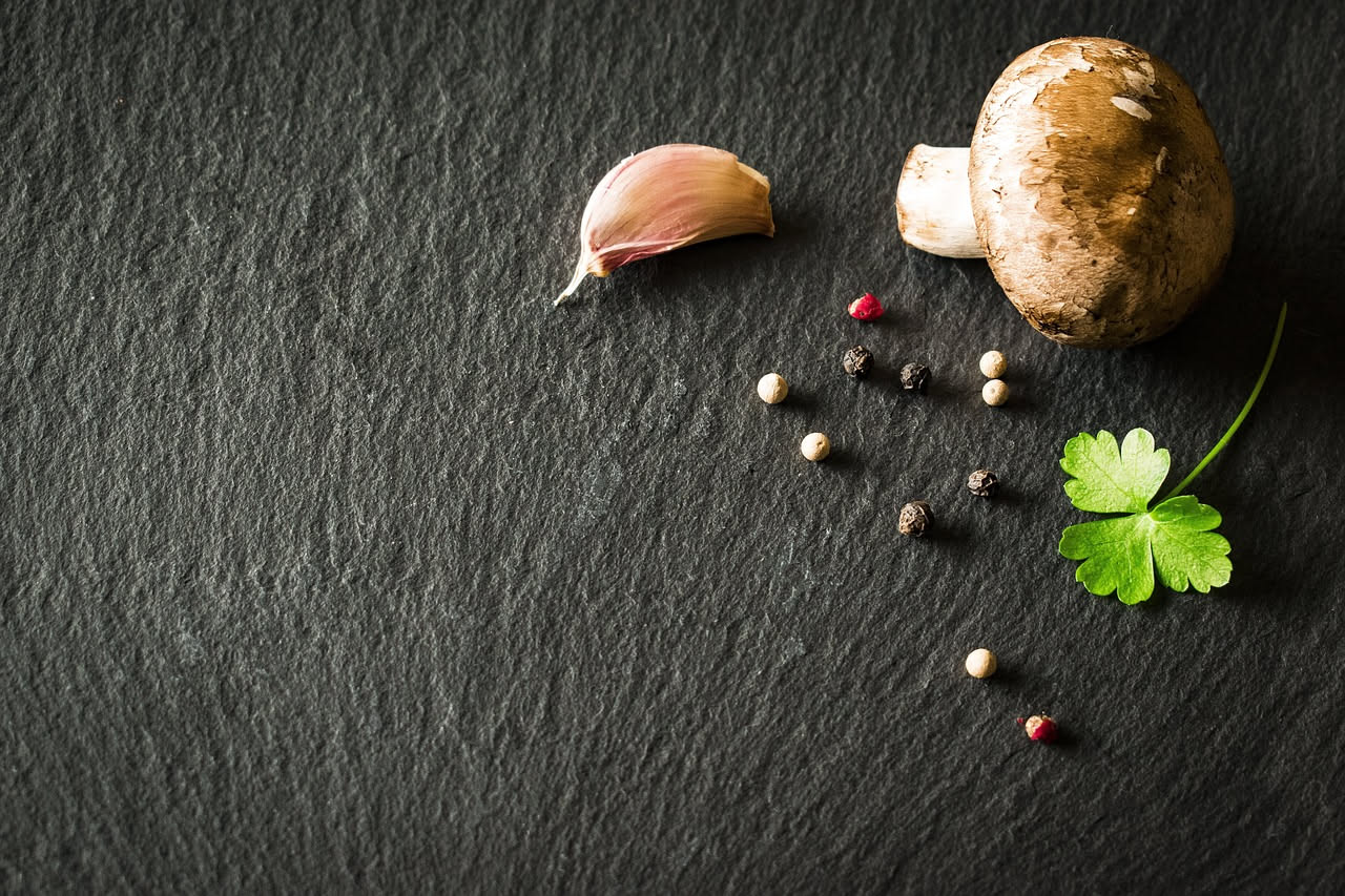 Ciotola di ceramica bianca con minestra di funghi fumante, funghi champignon e porcini visibili nel brodo, sedano e carota tritati, filo d'olio crudo, cucchiaio di legno sul piatto