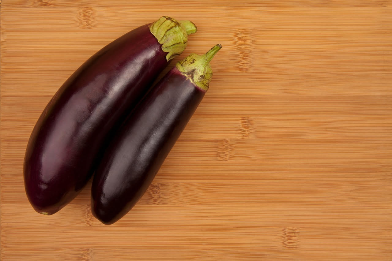 Ciotola bianca con minestra di melanzana: melanzane grigie e tenere galleggiano in brodo trasparente color oro, con foglioline di basilico verde brillante sparse in superficie e filo di olio d'oliva