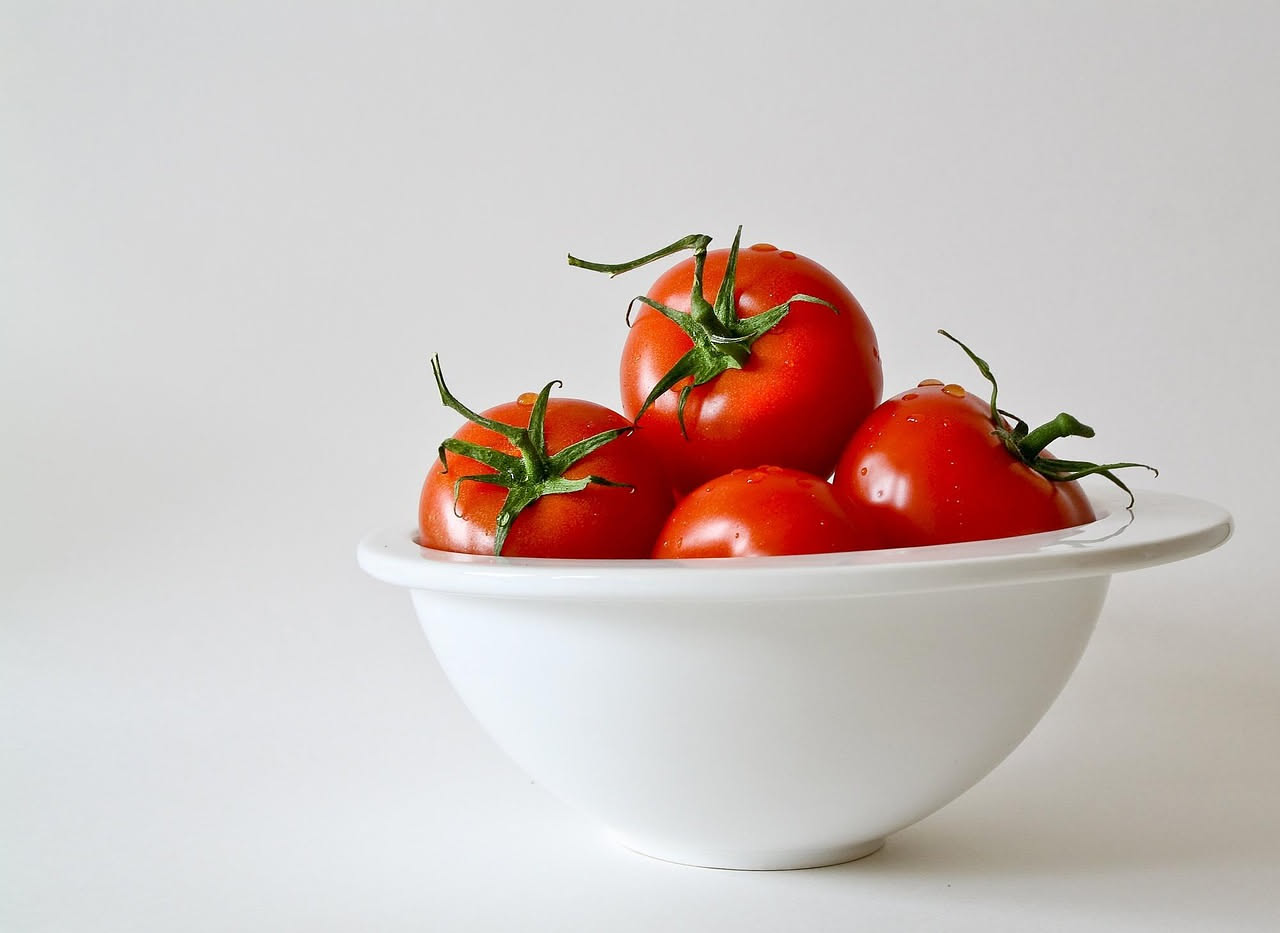Una ciotola bianca con minestra di pomodoro rosso intenso, con crostini di pane tostato in superficie, filo di olio verde oliva, basilico fresco e cucchiaio di ceramica