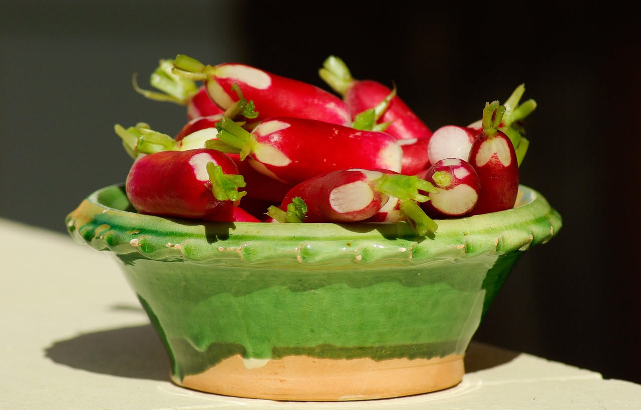 Minestra di ravanelli in ciotola di ceramica bianca con brodo trasparente ambrato, fettine di ravanello rosa e bianche, cipolla ammorbidita, prezzemolo fresco verde intenso tritato in superficie, cucc