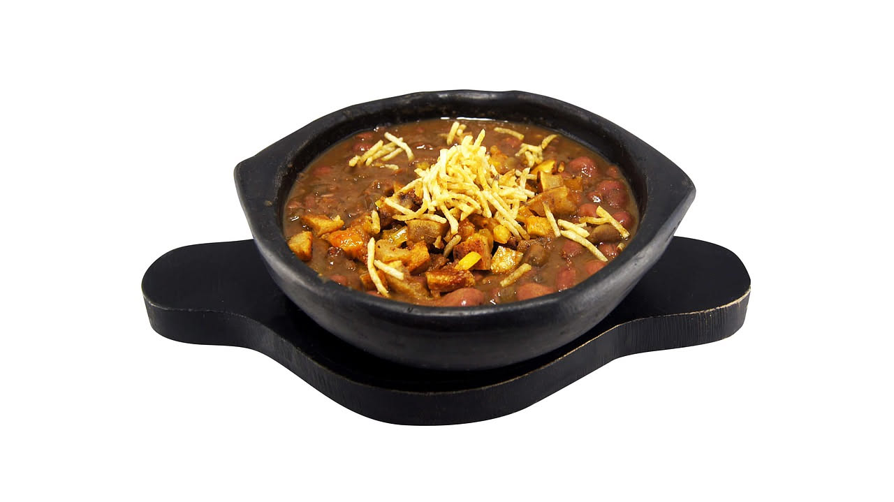 Una ciotola di minestra di risu e fagioli con riso bianco e fagioli scuri in brodo cremoso, decorata con olio di oliva e prezzemolo fresco