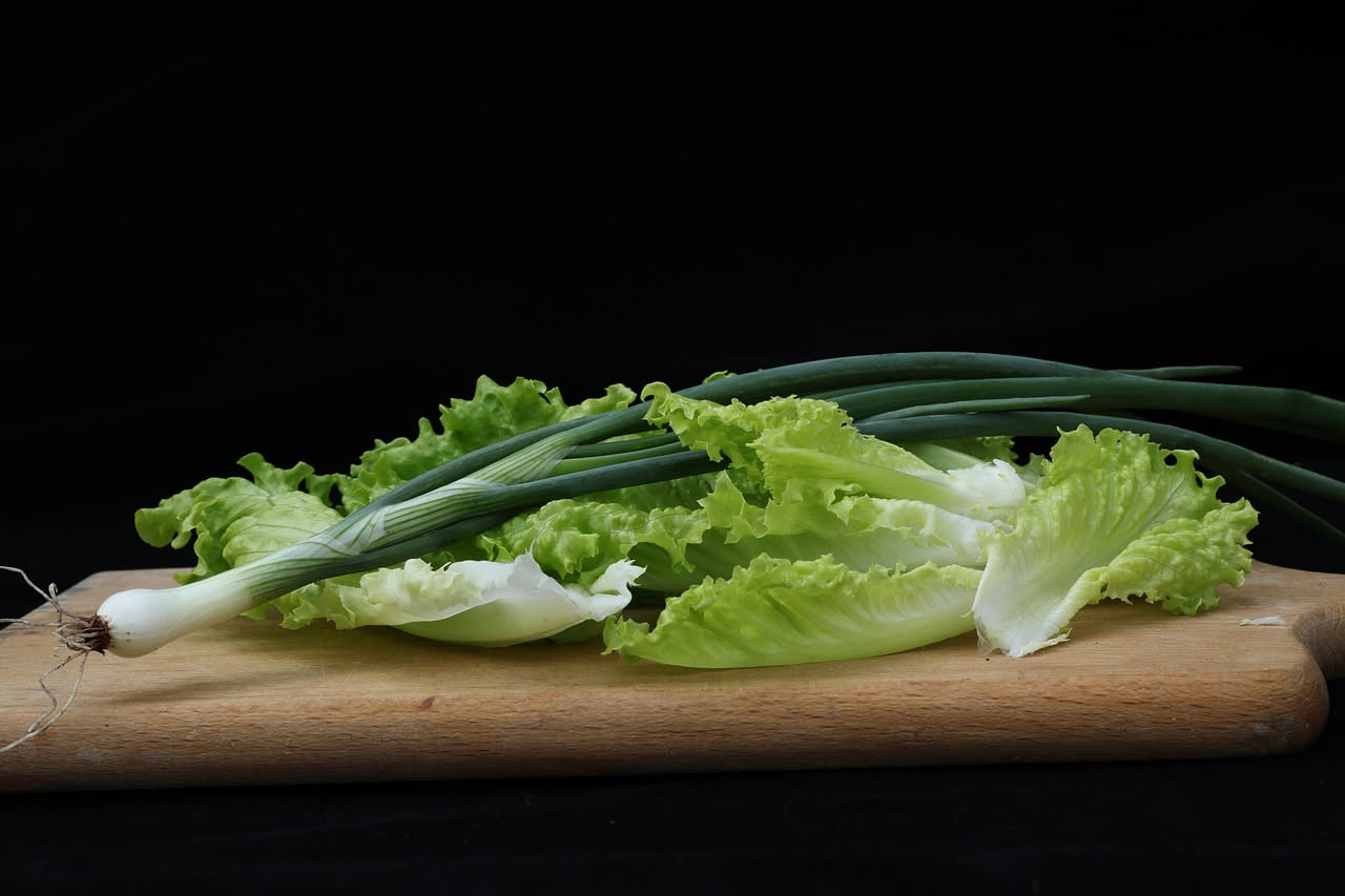 Una ciotola di ceramica bianca ricolma di minestra: scarole verde scuro leggermente appassite, fagioli bianchi cremosi sparsi nel brodo trasparente e leggermente dorato, filo di olio d'oliva in superf