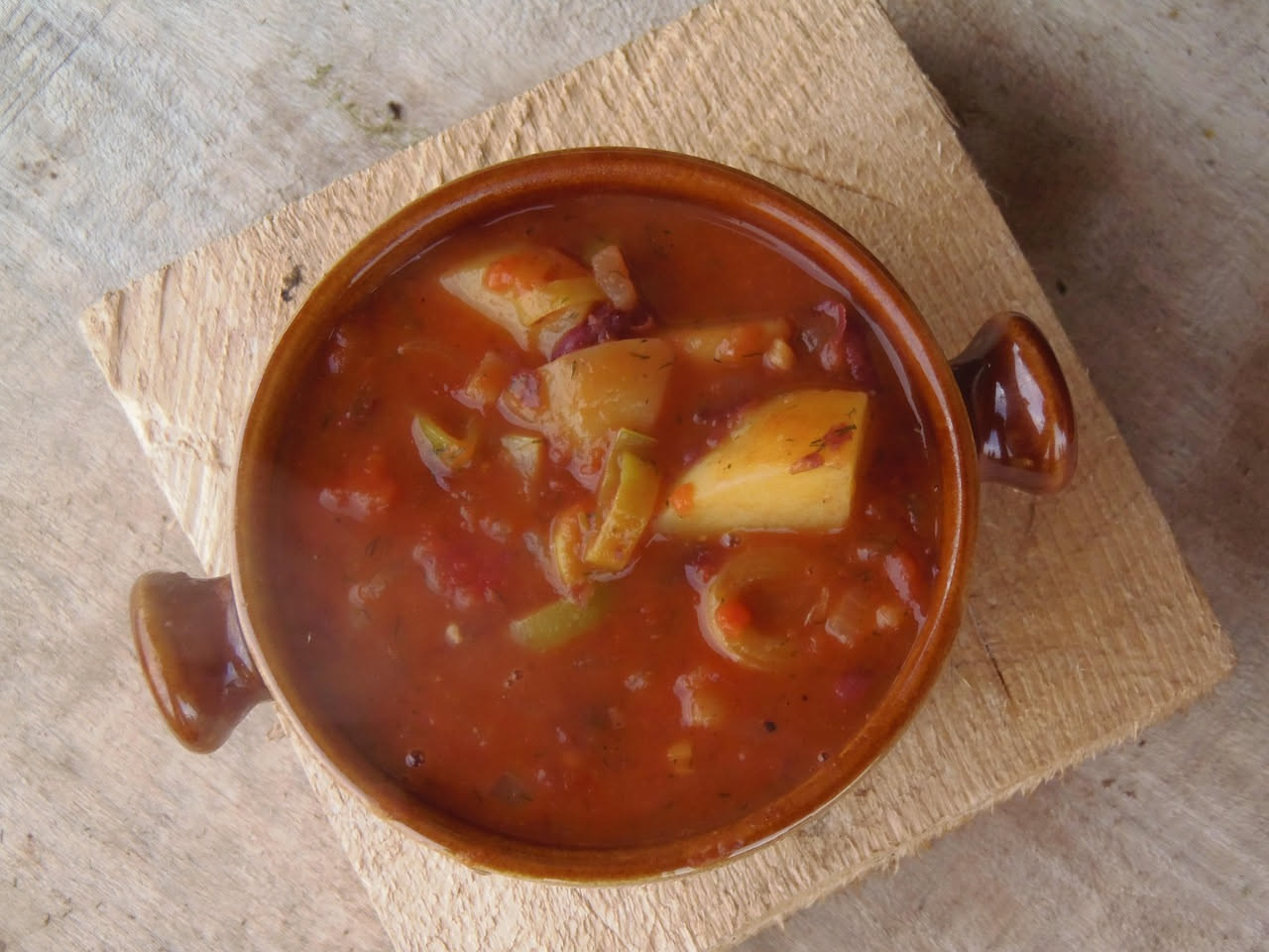 Una zuppiera di ceramica bianca piena di minestra maritata: brodo trasparente ambrato, verdure tagliate a pezzi regolari tra cui cavolo verde, scarola, cicoria, carote arancioni e sedano, pezzetti di