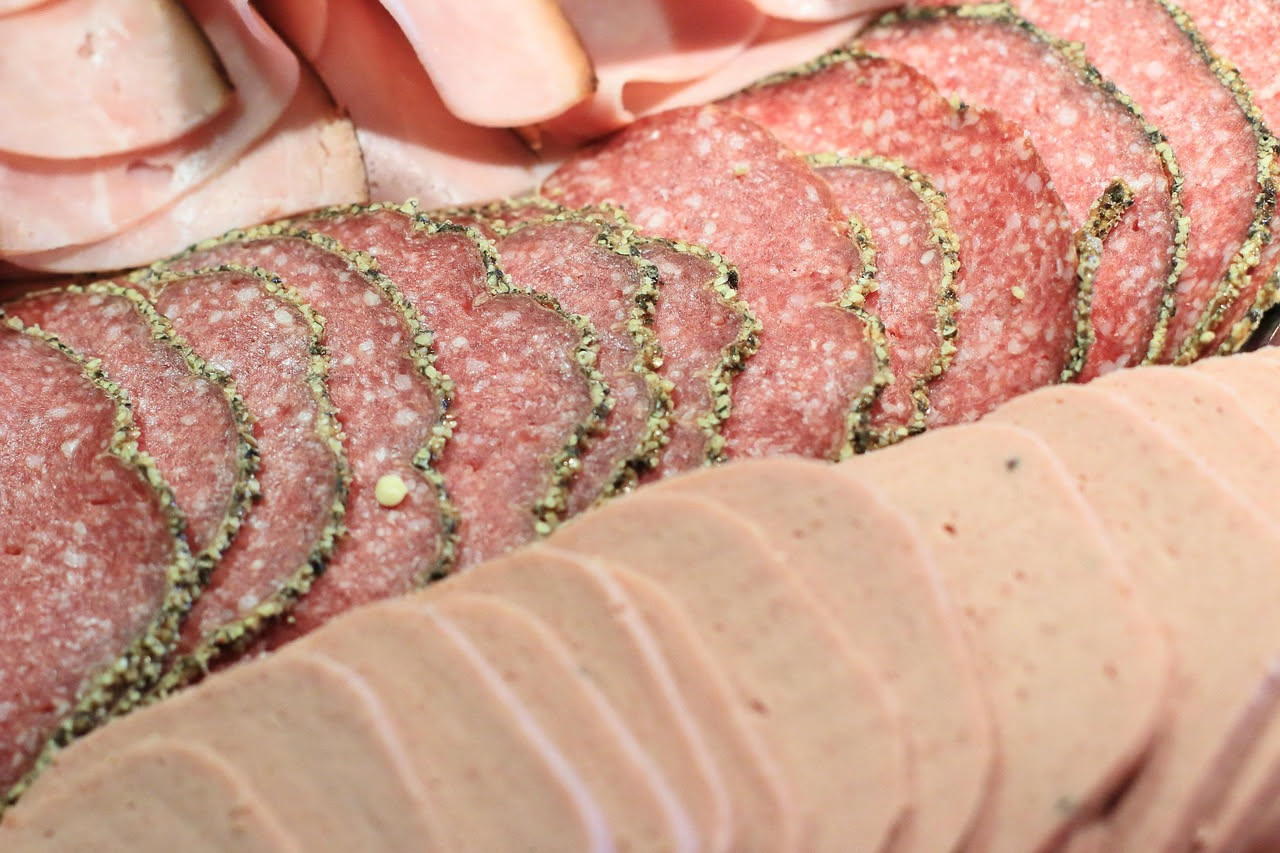 Fette di mortadella di Amatrice tagliate finemente, rosate con venature di grasso bianco, su un tagliere di legno con un coltello affilato