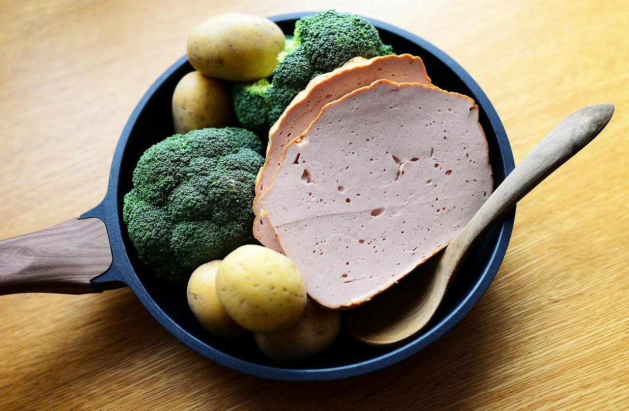 Mortadella affettata finemente disposta su un piatto bianco con bordo azzurro, con grani di pepe nero visibili e sfondo neutro