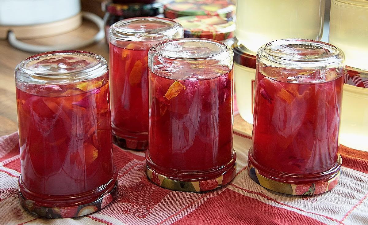 Vasetti trasparenti di mostarda di Cremona con frutta candita visibile dentro, disposti su una superficie di legno chiaro accanto a un coltello e una pera fresca