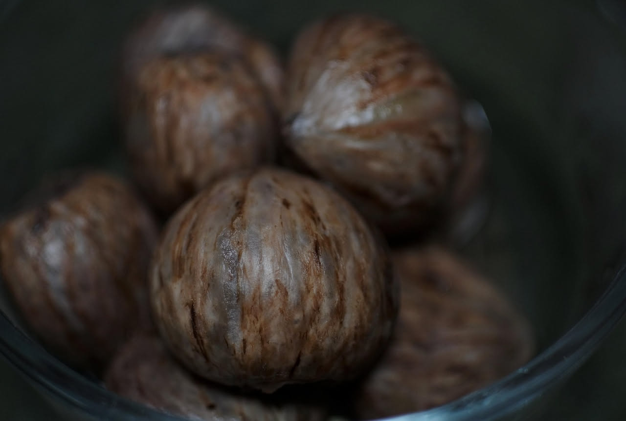 Noci intere ricoperte di sciroppo trasparente e lucido, disposte su un piatto bianco. Lo sciroppo forma una patina densa e brillante attorno a ogni noce, con sfondo di barattolo di vetro aperto.