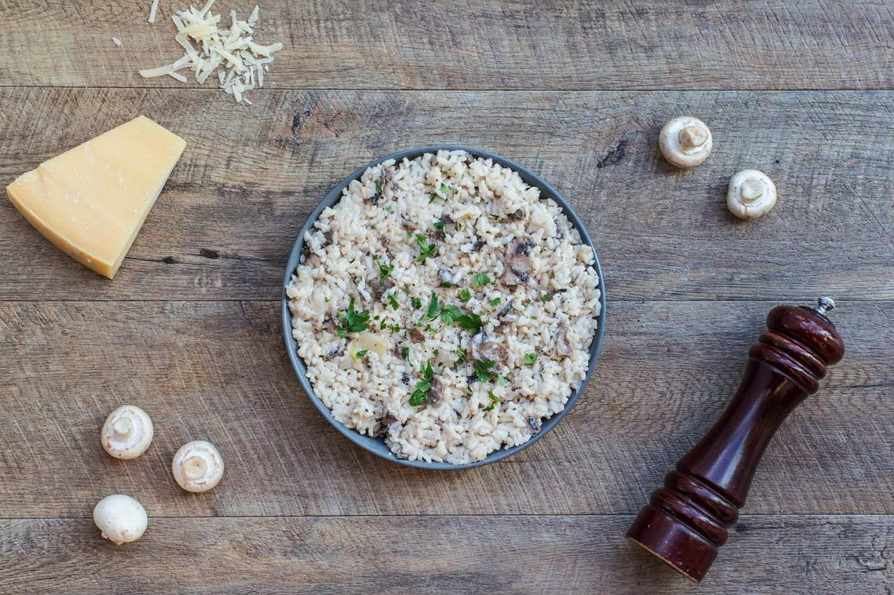 Piatto di orzotto cremoso color beige con funghi marroni e bianchi sparsi in superficie, guarnito con prezzemolo verde e un filo d'olio d'oliva, servito in un piatto bianco fondo